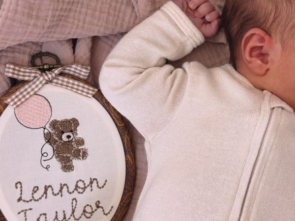 Baby announcement photo: embroidered 'Lennon Taylor' hoop beside newborn Lennon Taylor Lautner