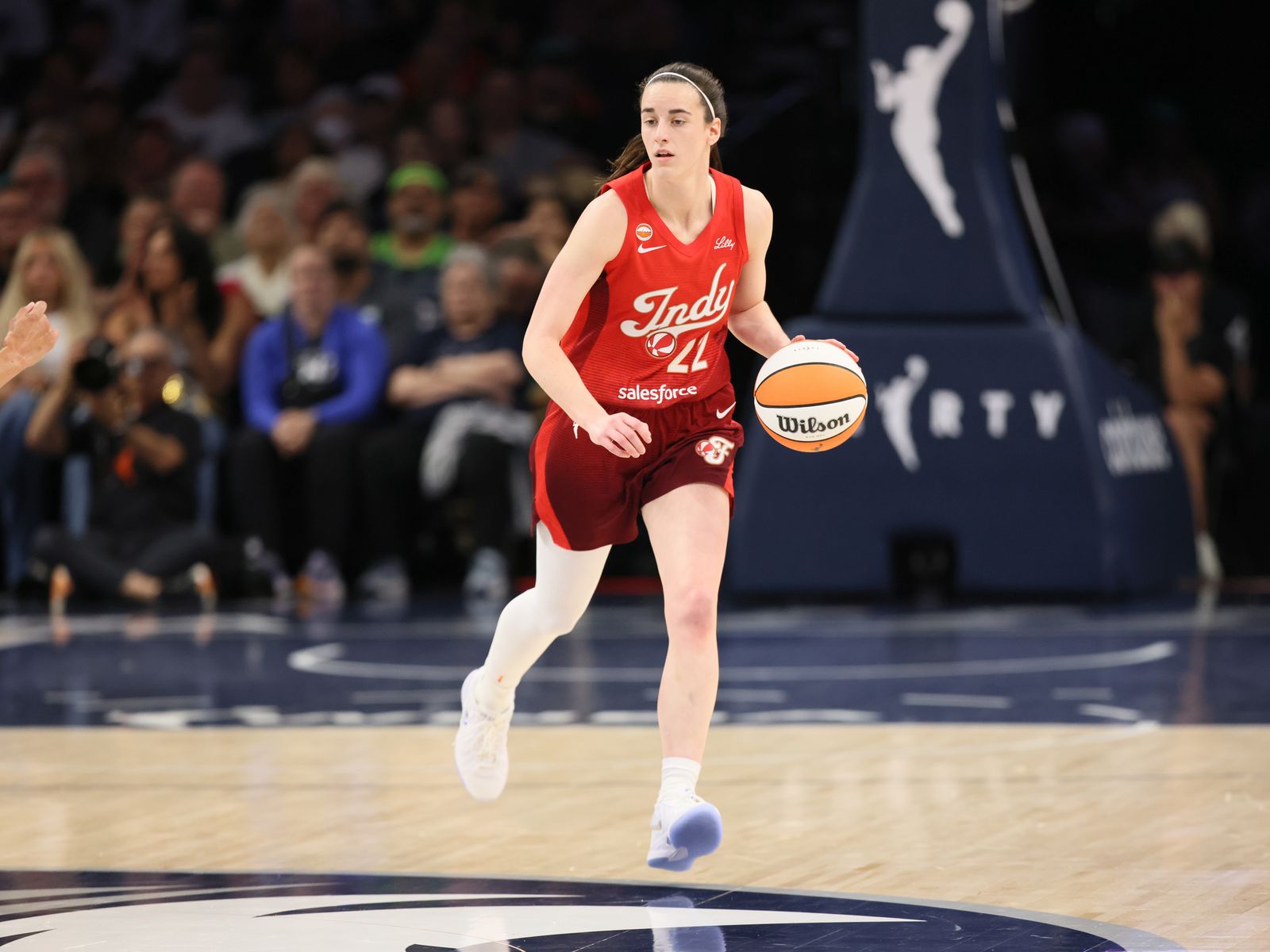 Caitlin Clark dribbling the basketball for the Indiana Fever in a red Indy uniform
