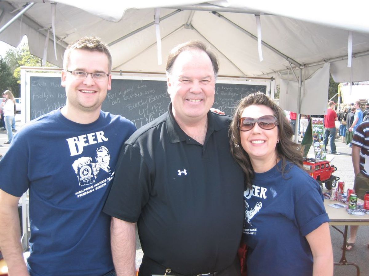 Dennis Haskins smiling and posing with two fans at an outdoor event