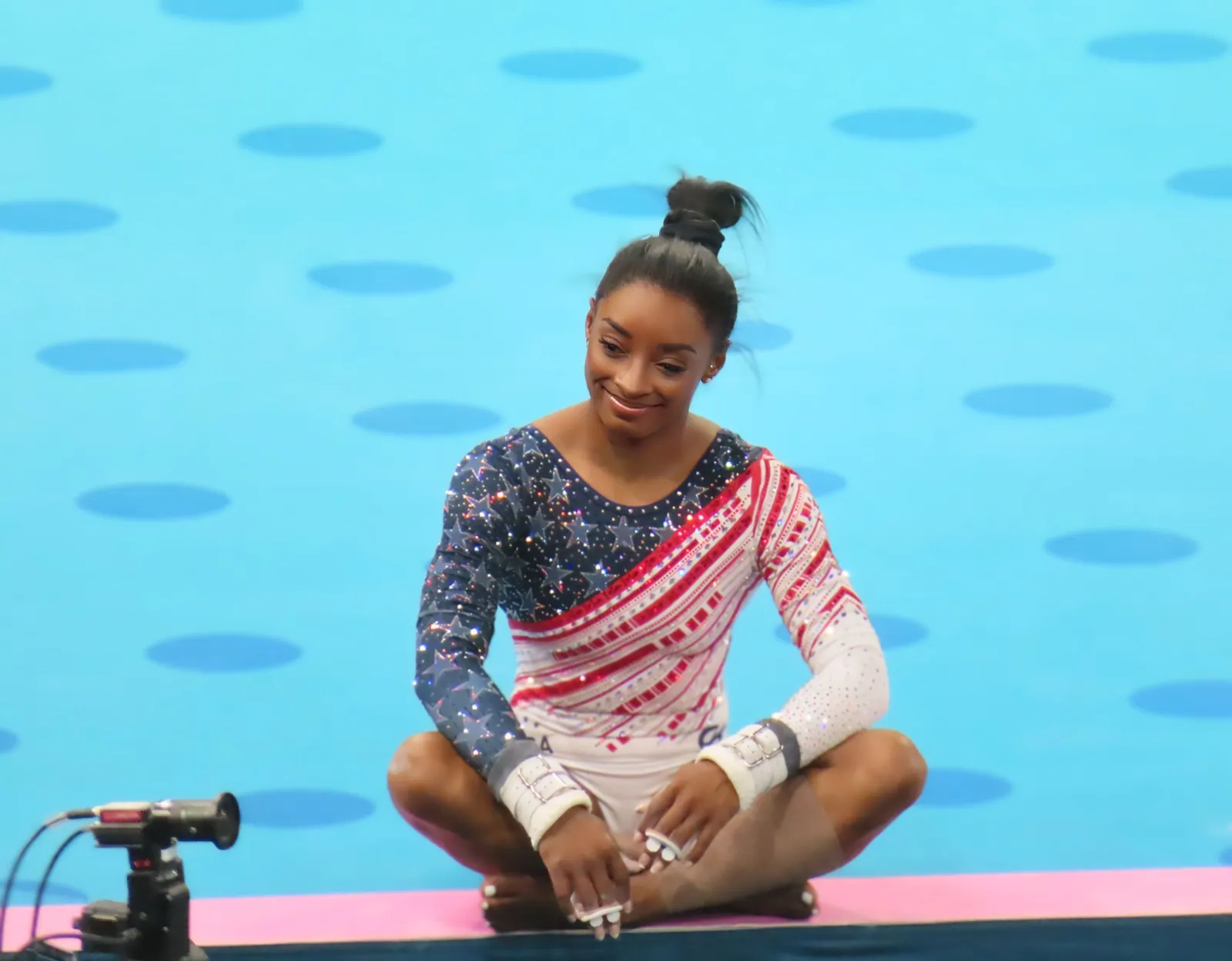 Simone Biles sitting on the competition floor at the Paris 2024 Olympics in a Team USA leotard