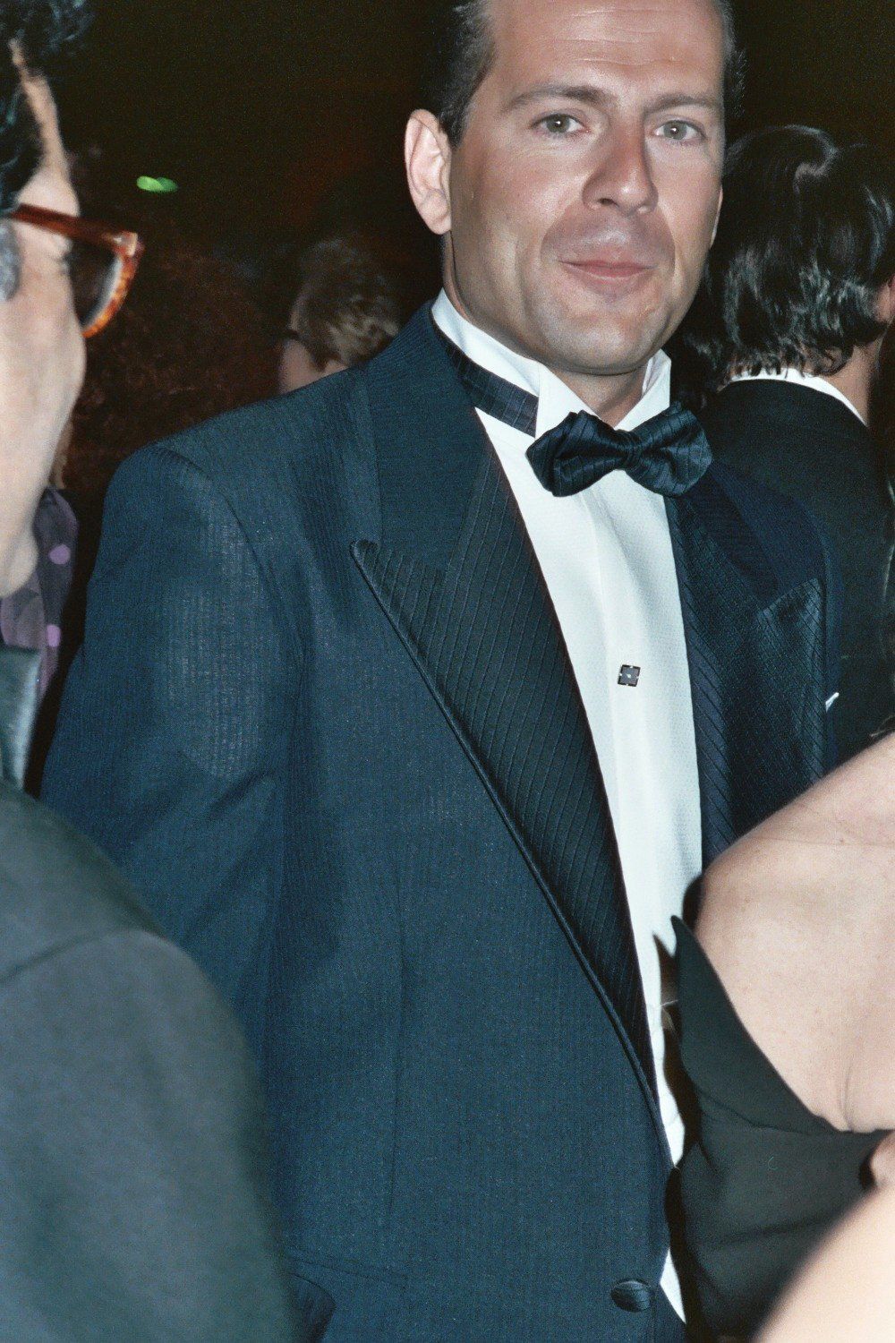 A young Bruce Willis in a tuxedo and bow tie at a red carpet event in the early 1990s