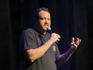 Shane Gillis performing stand-up on stage with a microphone