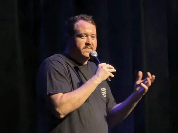 Shane Gillis performing stand-up on stage with a microphone