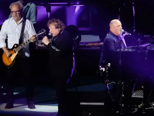 Lou Gramm singing on stage with Mick Jones and Billy Joel during a 2018 concert