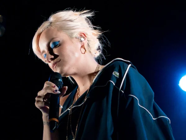 Lily Allen performing on stage at the El Rey Theatre in Los Angeles in 2018, holding a microphone under blue stage lights