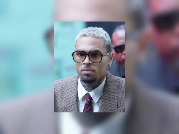 Chris Brown arriving at court in London in 2025, wearing glasses, a checked suit and a tie.