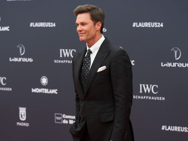 Tom Brady smiling on the red carpet at the 25th Laureus World Sports Awards in a black suit