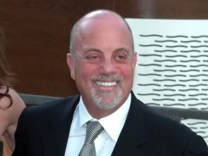 Billy Joel smiling in a dark suit and tie at the Metropolitan Opera in 2009