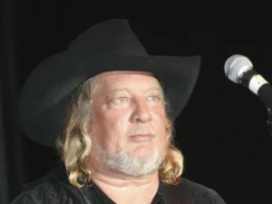 Country singer John Anderson in a black cowboy hat performing on stage with a guitar