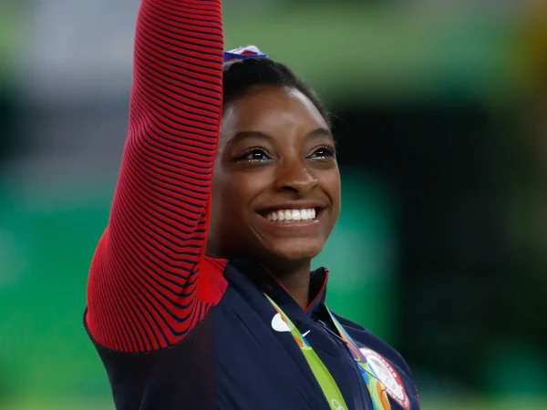 Simone Biles smiling with her gold medal at the Rio 2016 Olympics all-around podium ceremony.