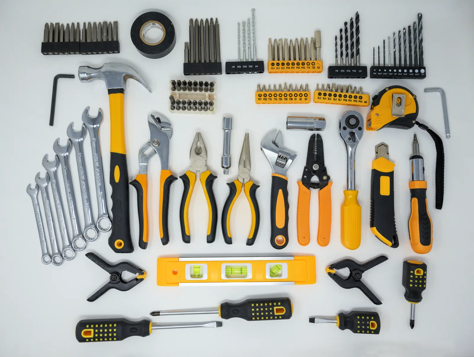 Hand tools including screwdrivers, pliers, wrenches, a tape measure and a level arranged on a white surface — the same kinds of tools stuffed into the Home Depot holiday sweater's apron pockets