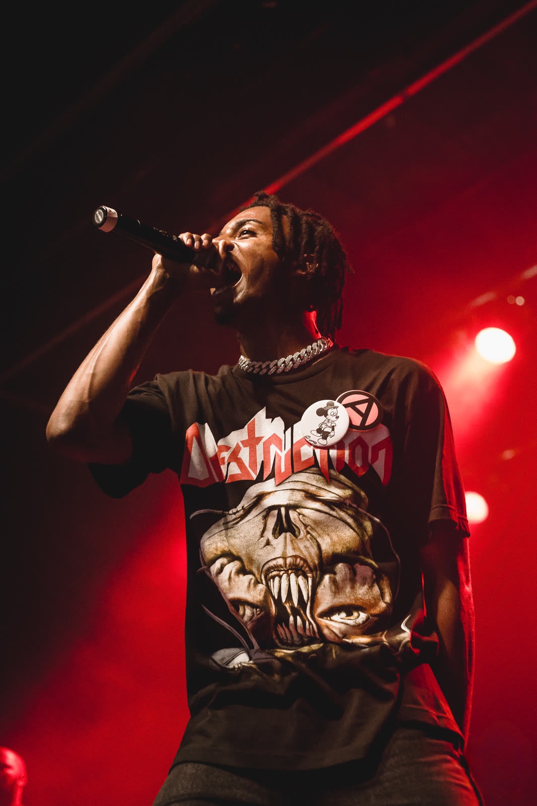 Playboi Carti performing live on stage, holding a microphone under red lights