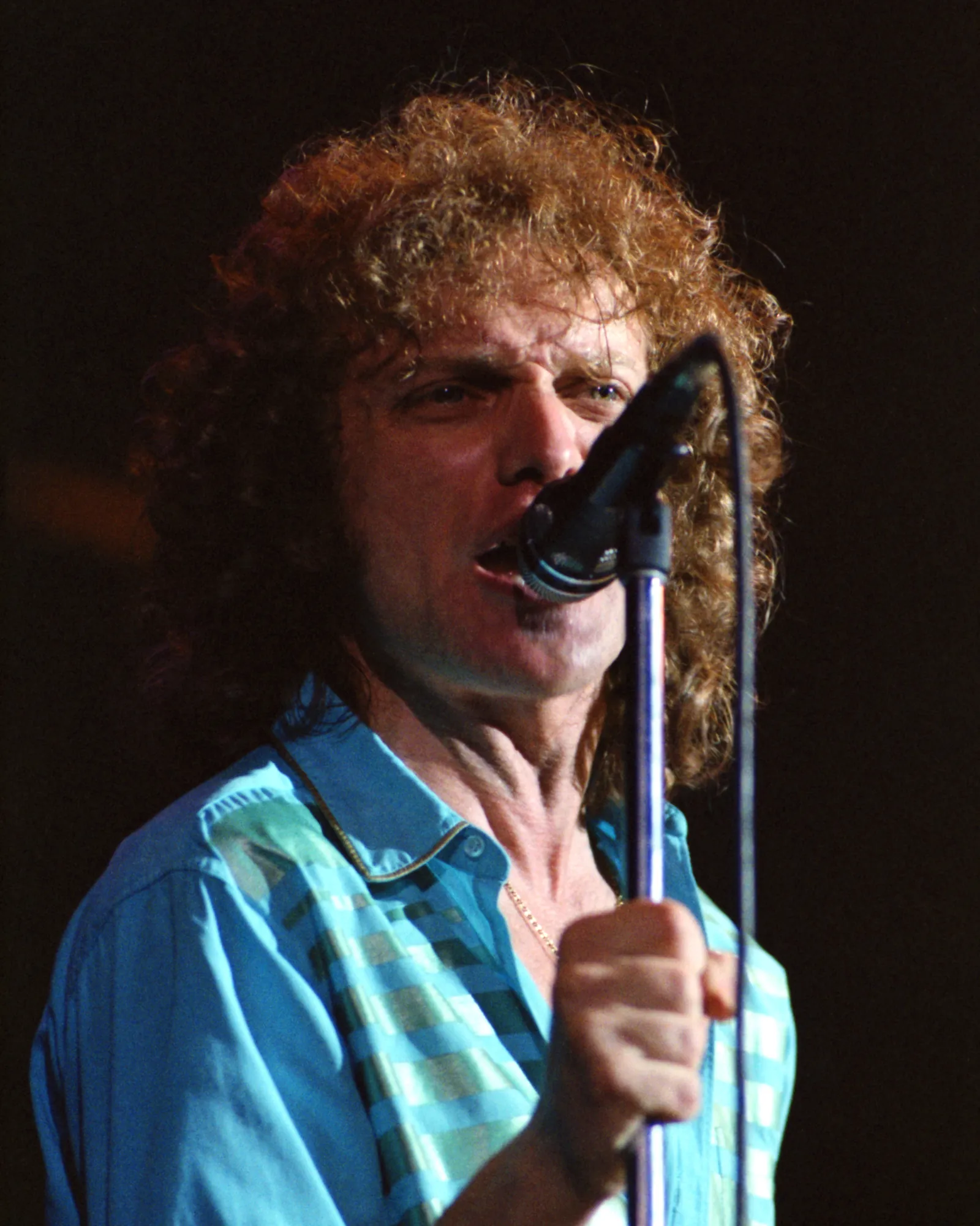 A young Lou Gramm with curly hair singing into a microphone during a 1979 Foreigner concert