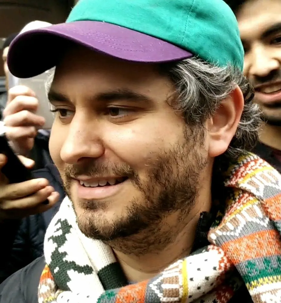 Ethan Klein smiling at a public appearance wearing a cap and scarf