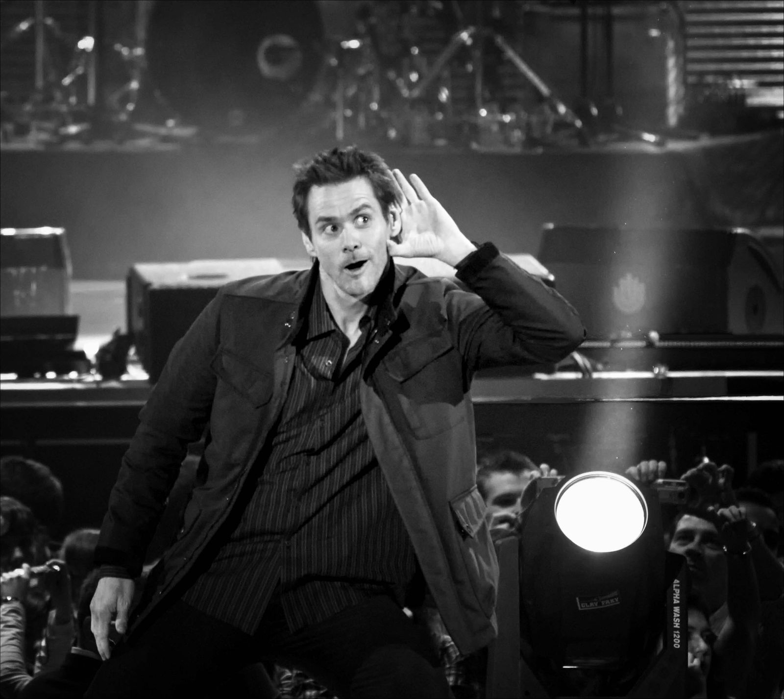 Jim Carrey performing on stage in 2008, hand raised to his ear in a playful gesture