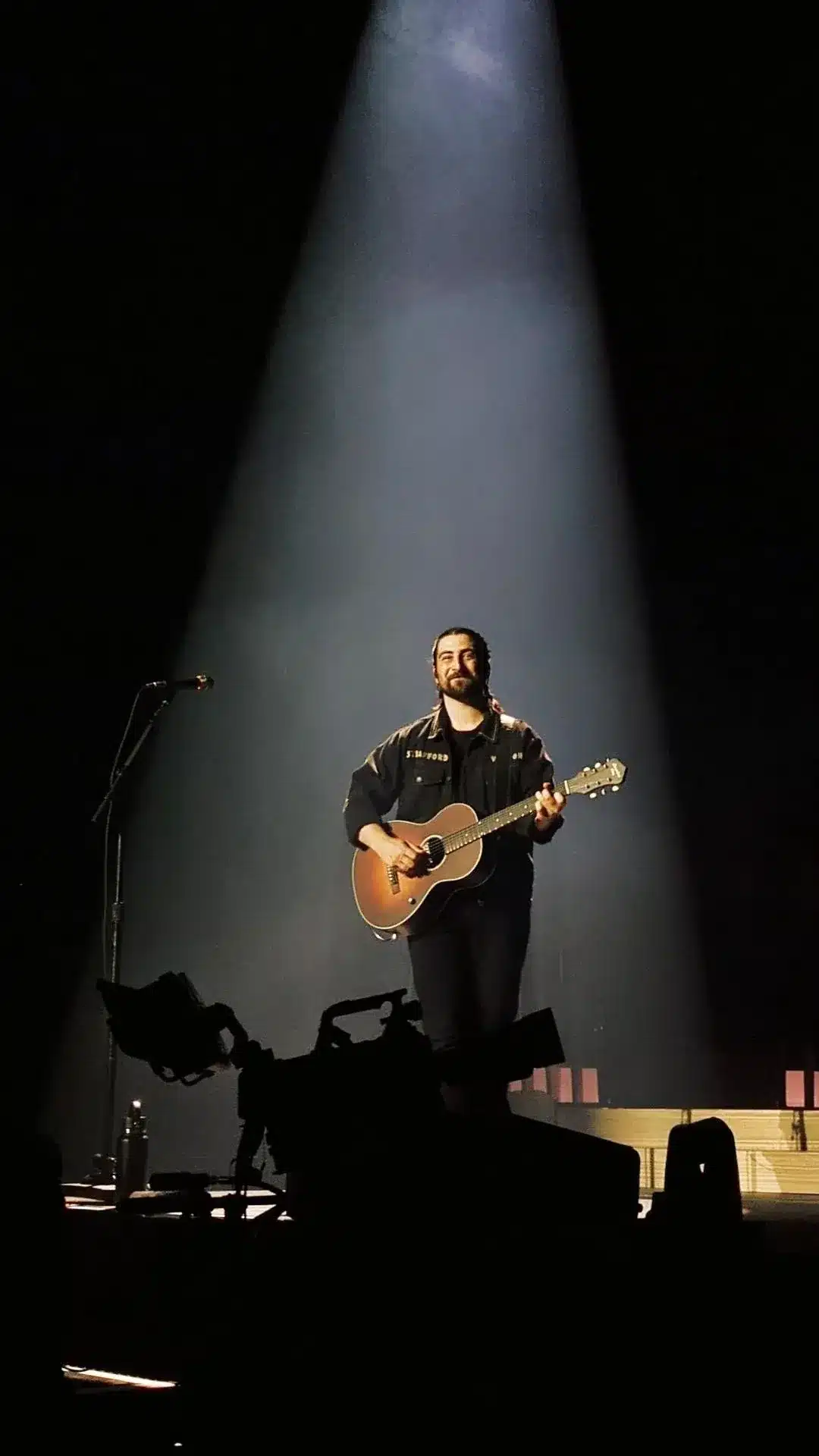 Noah Kahan performing on stage under a spotlight in 2024