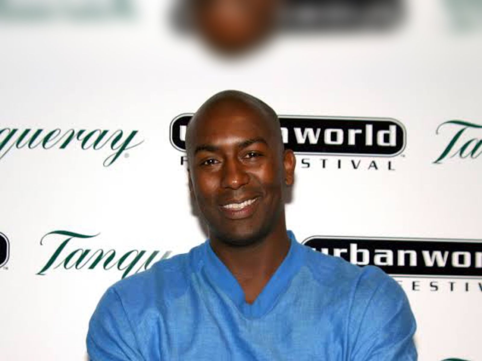 Reggie McFadden smiling in a blue shirt with arms crossed at a festival step-and-repeat backdrop.