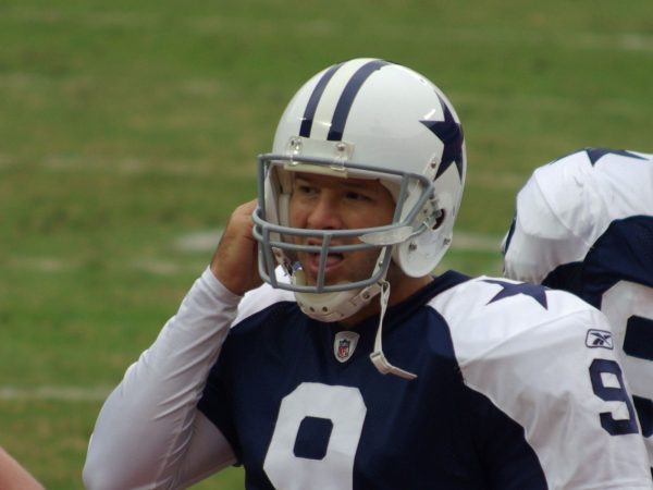 Tony Romo in a Dallas Cowboys helmet adjusting his gear on the sideline