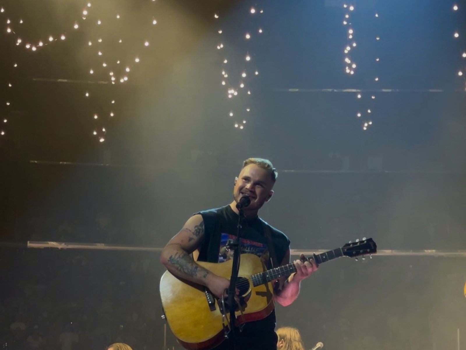 Zach Bryan performing on stage with an acoustic guitar, his full head in frame